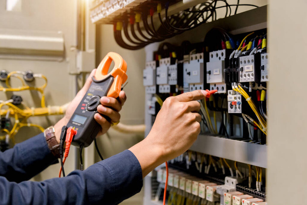 Инженер-электрик работает измерителем напряжения и тока электрической линии в электрическом шкафу управления. - Фото, изображение
