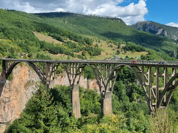  Picturesque Djurdzhevich Bridge. Montenegro. Reinforced concrete arch bridge over the Tara river. Mountains surrounding the canyon. Forests on the slopes of the mountains. Blue sky over the mountains.   - Fotografie, Obrázek