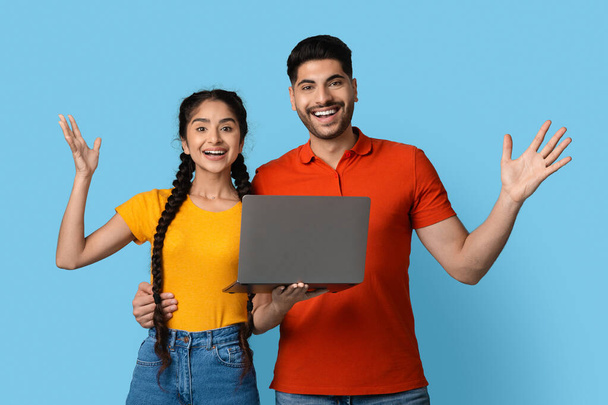 Возбужденная молодая ближневосточная пара с ноутбуком позирует над синим фоном - Фото, изображение