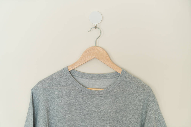 grey t-shirt hanging with wood hanger on wall - Foto, Bild