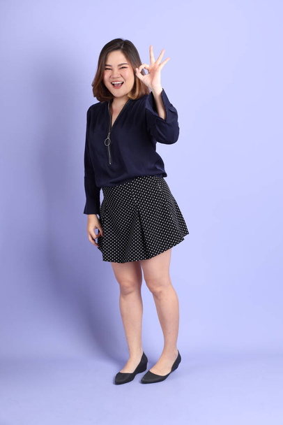 The chubby Asian woman standing on the purple background with the casual clothes. - Фото, изображение