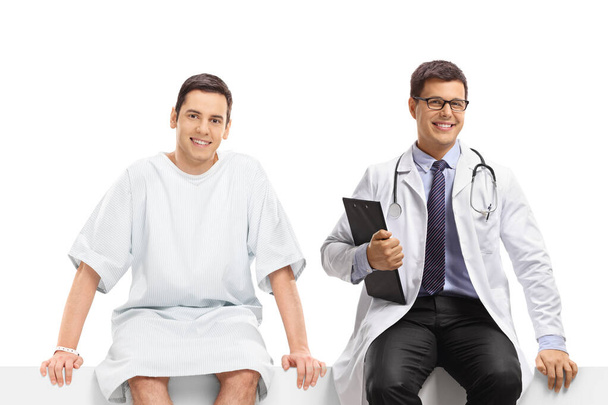 Male doctor and a young male patient sitting on a panel isolated on white background - Foto, Bild