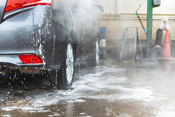 Lavado manual con jabón blanco, espuma en el cuerpo. Lavado de coches usando agua de alta presión. - Foto, imagen