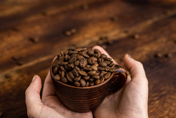 Coffee beans in a cup in female hands on a brown background. - Foto, Bild