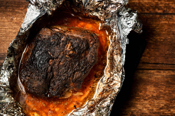 A large piece of baked meat with spices wrapped in foil in the oven. - Zdjęcie, obraz