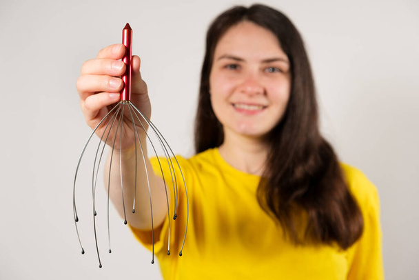 A woman with a metal flexible massager for self-massage of the head on a white background, copy the place for the text - Photo, image