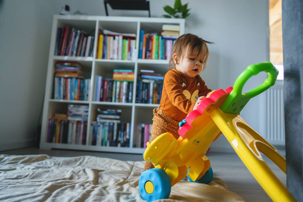 Jedno małe dziecko rasy kaukaskiej w wieku sześciu lub siedmiu miesięcy bawiące się zabawką na podłodze w domu w samym pokoju - dziewczynka dobrze się bawiąca badając nową zabawkę dorastając w prawdziwym świecie koncepcja kopiuj przestrzeń - Zdjęcie, obraz