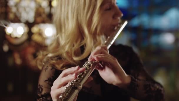 Erwachsene blonde Frau spielt Flöte auf einem Hintergrund aus Buntglasfenstern - Filmmaterial, Video