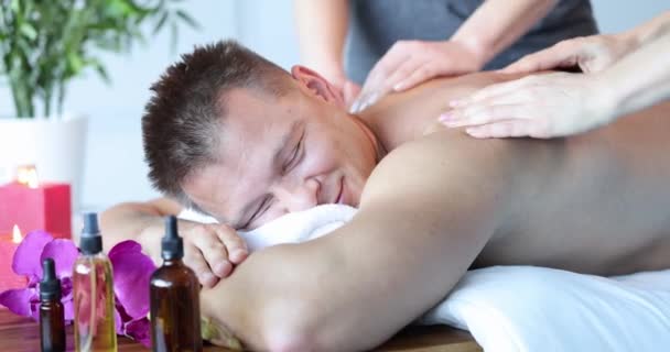 Two masseuses give back massage to happy young man - Felvétel, videó