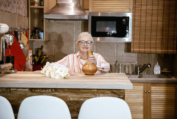 Χαρούμενη ηλικιωμένη γυναίκα που στολίζει ένα βάζο για το σπίτι της. - Φωτογραφία, εικόνα