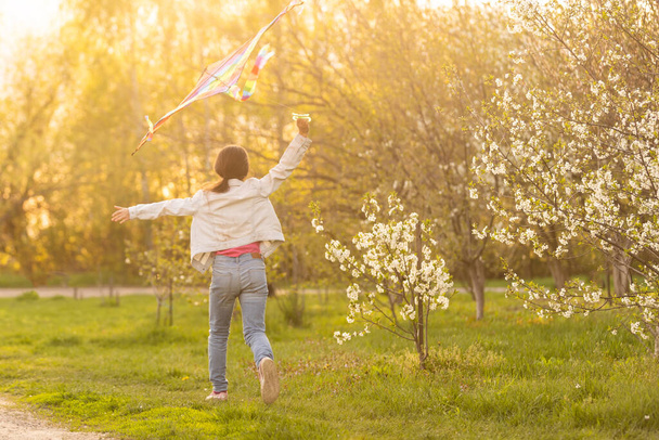Happy little girl running with kite in hands on the beautiful field at sunrishe time - Фото, зображення