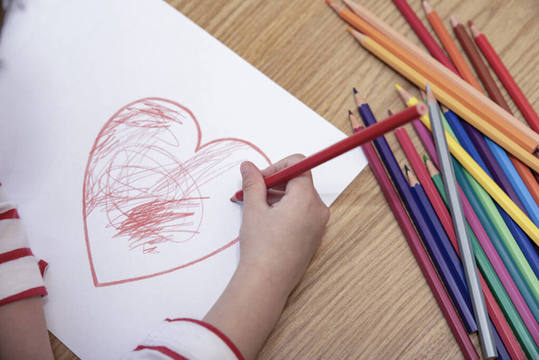 Little girl on the floor, colouring a red heart for father's day. - Фото, изображение