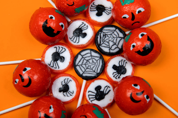 Halloween snoep met zwarte spinnen, spinnenweb, lachende en boze pompoenen op oranje achtergrond, bovenaanzicht - Foto, afbeelding