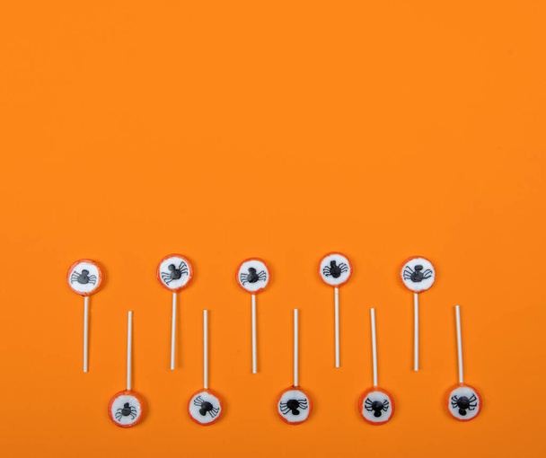 Halloween candy row with black spiders and cobweb on orange color background,top view - Photo, image