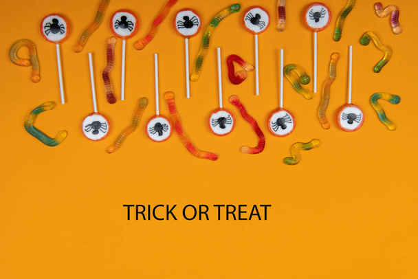 Halloween candy with black spiders,cobweb and tasty jelly worms on orange color background,trick or treat - Photo, Image