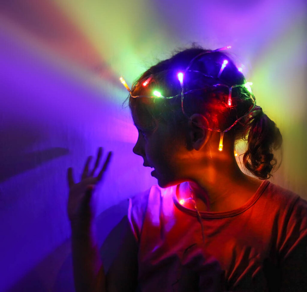 A girl holds beautiful bright lights in her hands. Child playing with magic lights at home. - Photo, Image
