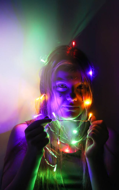 A girl holds beautiful bright lights in her hands. Child playing with magic lights at home. - Photo, Image