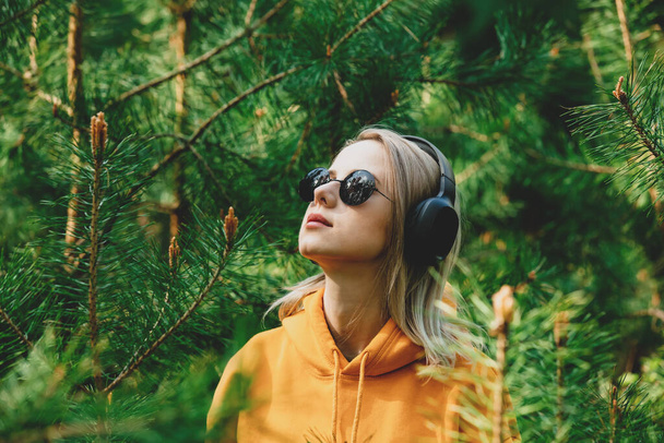 Κομψό κορίτσι με κουκούλα ακούστε μουσική στα ακουστικά στο πευκοδάσος - Φωτογραφία, εικόνα