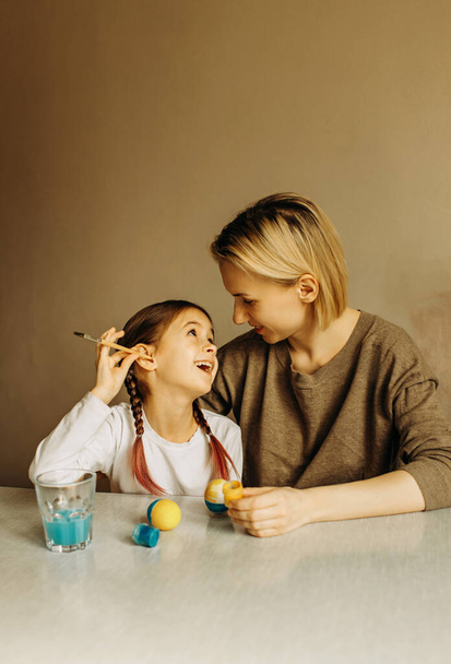 Portrait of a mother and daughter painting an egg in blue and yellow. Ukrainian family is preparing for Easter. The egg is painted in the color of the flag of Ukraine. - Photo, image