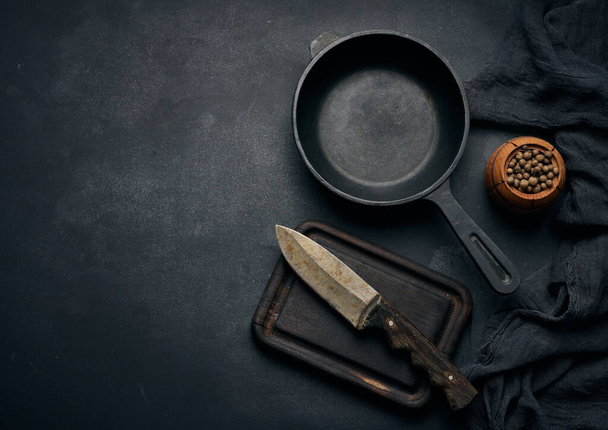 Empty round cast iron frying pan with wooden handle on black table, top view - 写真・画像