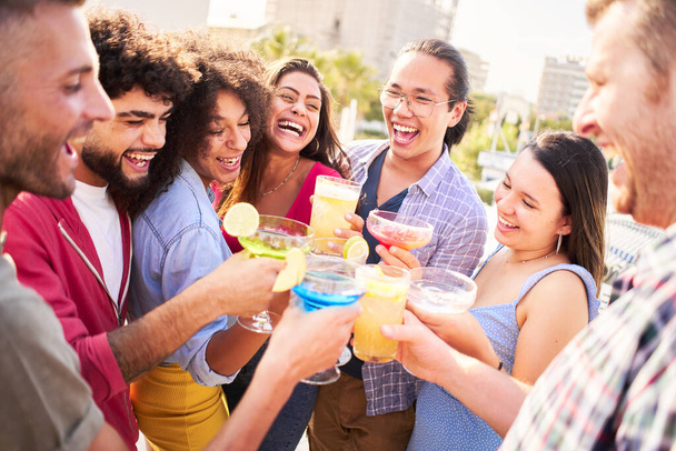 Group of happy friends drinking and toasting cocktails at brewery bar rooftop terrace restaurant. Friendship concept with young people having fun. - Photo, Image