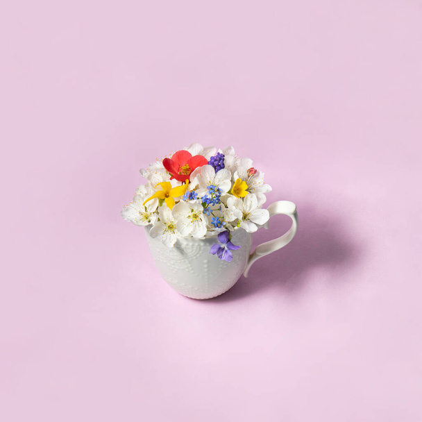 Colorful spring flowers in white cup on pastel light blue background. Creative flowers concept. Minimalistic nature composition with copy space. Spring tea idea. - Photo, Image