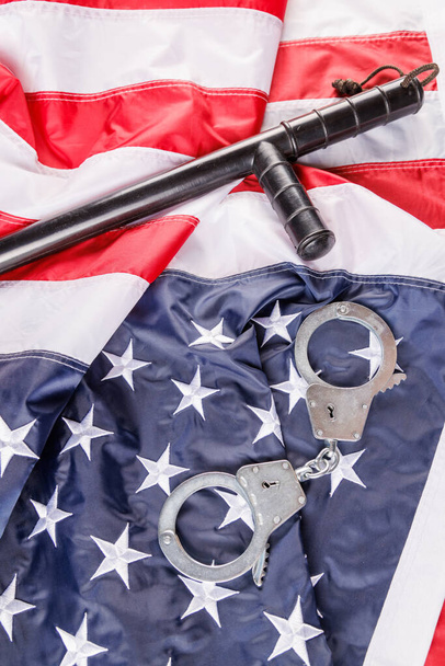 серебряные металлические наручники и полицейская дубинка над флагом США на плоской поверхности - Фото, изображение