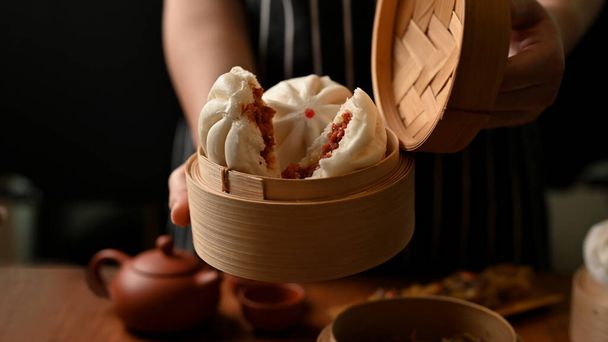 Female chef holding a bamboo steamer with tasty original Chinese steamed pork buns. Asian restaurant cuisine. - Foto, imagen