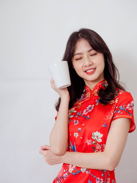 Portrait of young asian woman wearing traditional cheongsam qipao dress relaxing drinking on white background. - Photo, image