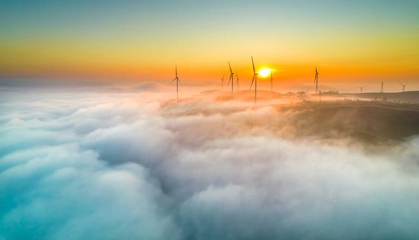 Aerial view top hill at dawn with fog covering small village in valley, beautiful wind power poles rising high to welcome a peaceful new day in highlands Da Lat, Vietnam - Foto, immagini