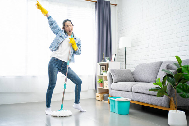 Mujer asiática divirtiéndose mientras hace tareas domésticas. Le gustaba cantar mientras limpiaba el suelo en la sala de estar.. - Foto, imagen