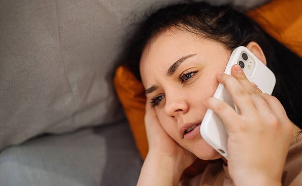 A sick girl with the flu in the bedroom at home. A sick young woman with a cold calls a doctor on the phone feeling unwell. - Fotoğraf, Görsel