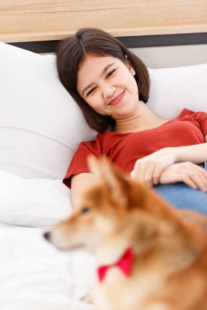 Little cute piękne inteligentne brązowy Shiba Inu pies sobie czerwony muszka leżące na bok strzegąc młody Azjatycki właściciel dziewczyna w casual strój leżąc na łóżku śpi w sypialni w rozmytym tle. - Zdjęcie, obraz
