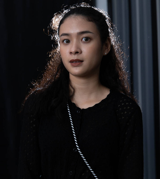 Portrait-Studioaufnahme von asiatischen jungen selbstbewussten lockigen Haaren weibliches Modell in lässigem Langarmshirt und Jeans mit Jeans mit Handtasche stehend lächelnd posierend Hand auf Hals Blick in die Kamera. - Foto, Bild