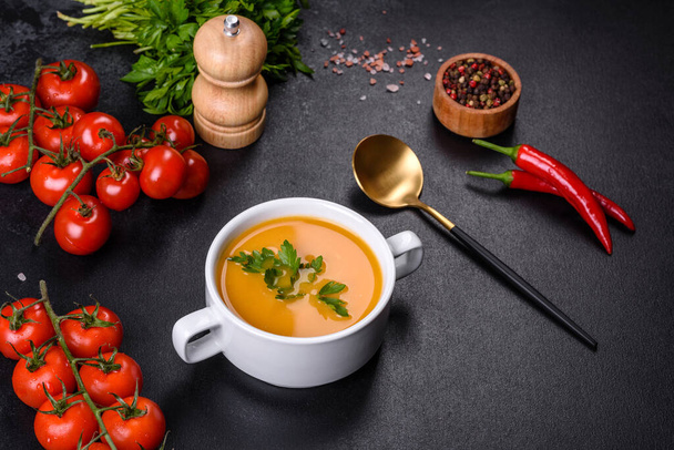 Delicious fresh pumpkin puree soup decorated with parsley in a white plate against a dark concrete background - Foto, afbeelding