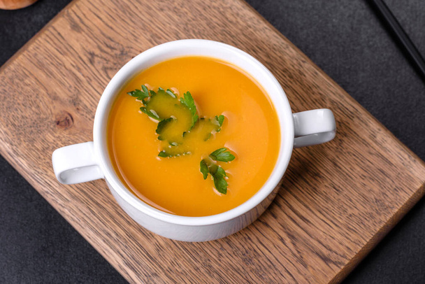 Delicious fresh pumpkin puree soup decorated with parsley in a white plate against a dark concrete background - Photo, Image