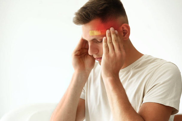 Mann mit medizinischem Pflaster auf der Stirn leidet unter Kopfschmerzen auf weißem Hintergrund - Foto, Bild
