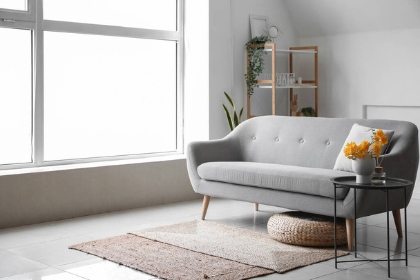 Interiér světlého stylového obývacího pokoje s pohodlnou pohovkou a vázou s květinami na stole - Fotografie, Obrázek