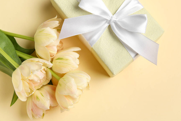 Beautiful flowers with gift box on beige background, closeup - Фото, изображение