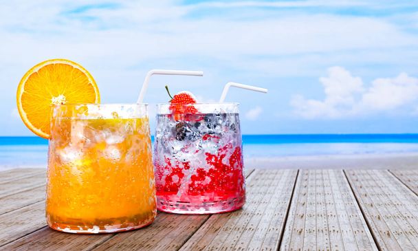 Апельсиновый сок в прозрачном стакане с кубиками льда и клубничным содом не смешивают алкоголь. Свежая клубника. Холодные напитки на деревянном балконе у моря посреди дня. 3D рендеринг - Фото, изображение