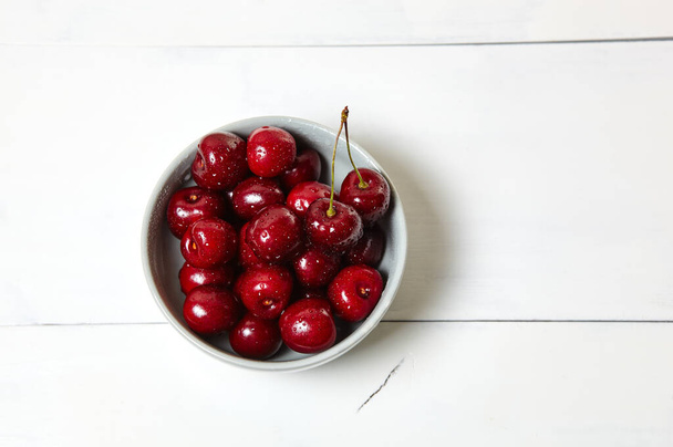 Sweet cherries in a ceramic bowl on wooden background, closeup. Fresh ripe sweet cherries in a bowl with droplets of water, top view - Foto, afbeelding