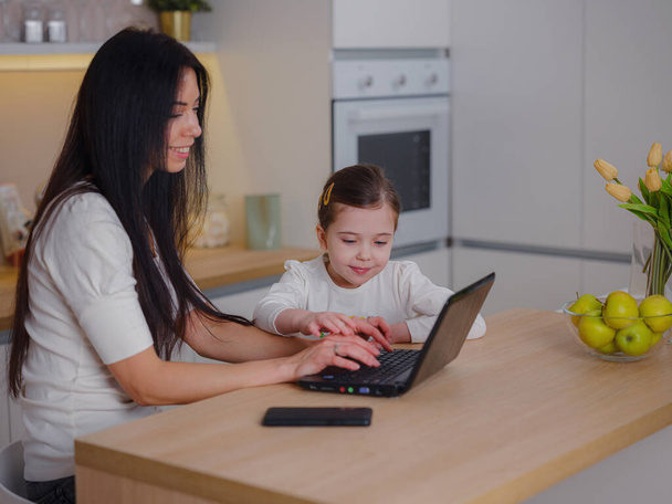 working mom works from home office. woman and child using laptop. Freelancer's workplace in cozy kitchen. Women's business, kindness, care. Lifestyle. - Photo, Image