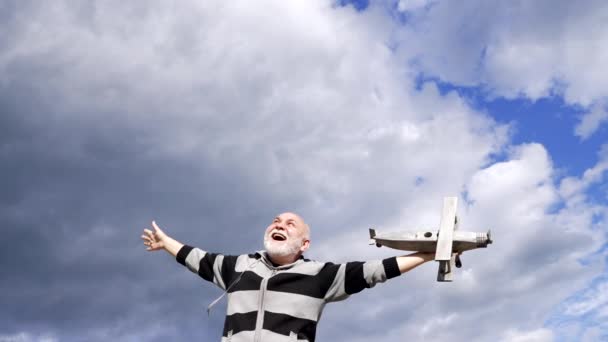 Happy senior man pretend flying on wooden airplane in sky, freedom - Video