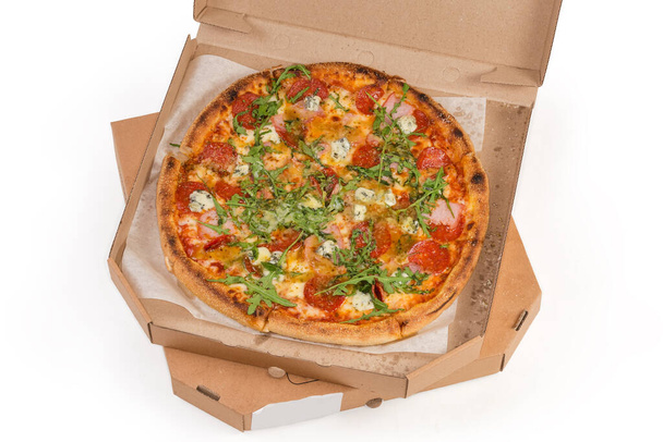 Στρογγυλή πίτσα με σαλάμι σε ανοιχτή συσκευασία με τη μορφή του ειδικού χαρτονένιου κουτιού βρίσκεται στο παρόμοιο κλειστό κουτί, πάνω όψη σε λευκό φόντο - Φωτογραφία, εικόνα