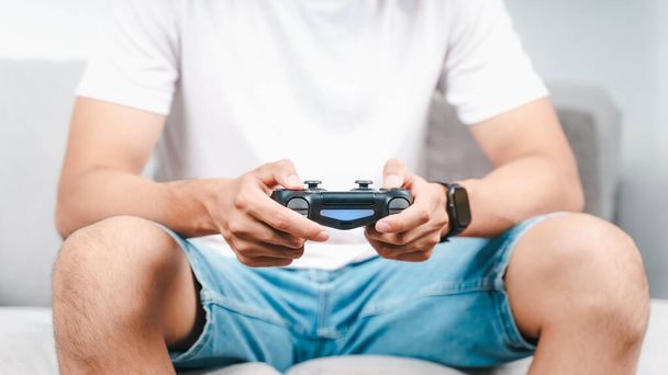 opgewonden jonge knappe man met joystick controller spelen video game zitten op de bank thuis - Foto, afbeelding