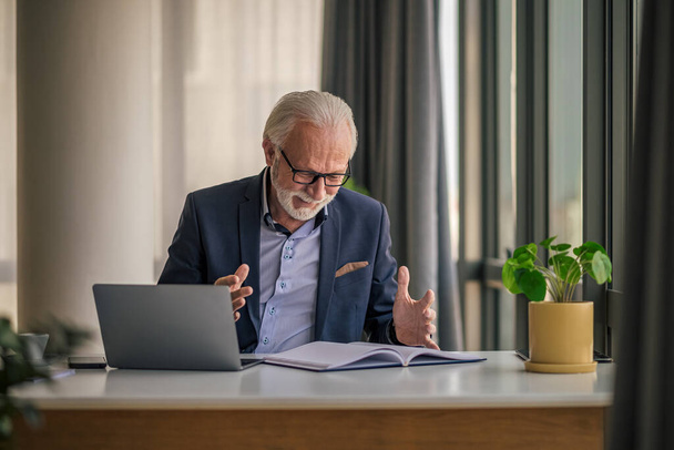 Happy senior entrepreneur gesturing and analyzing successful business plan, Male professional using laptop at desk, He is in formals at office. - Photo, image