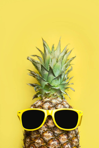 Summertime concept. Pineapple with yellow sunglasses and space for text over yellow background - Foto, afbeelding