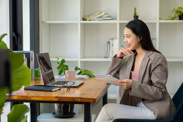 Sukces azjatyckiej bizneswoman używa komputera i Internetu do pracy w domu. Cute girl tworząc freelance wpisując na laptopie do czatu online, telekonferencje z klientami. - Zdjęcie, obraz