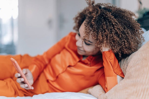 елегантна кучеряве волосся жінка лежить в ліжку перевірка мобільного телефону вид збоку
 - Фото, зображення