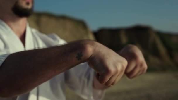 El hombre de judo confiado calentando las manos girando puños en la naturaleza al aire libre de cerca. Luchador de karate haciendo ejercicios de brazos de pie playa de arena. Atleta barbudo practicando la técnica marcial. Estilo de vida deportivo. - Imágenes, Vídeo